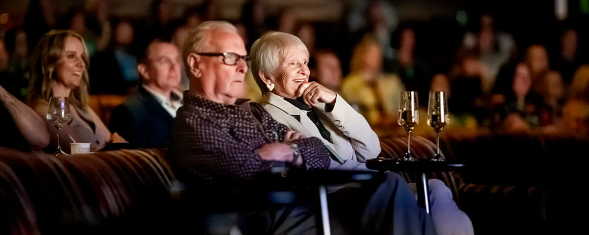 Glenys and Ian seated in Palladium, attentively watching a performance.