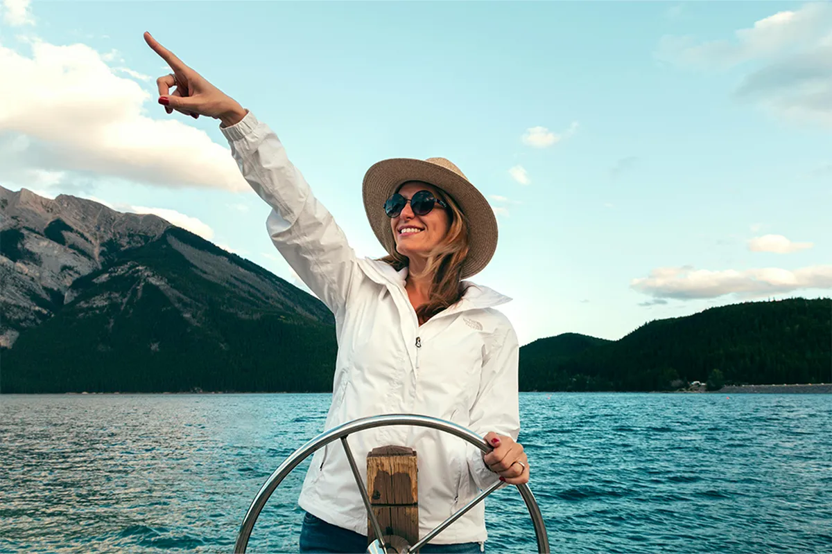 A woman in a white jacket and hat steers a boat