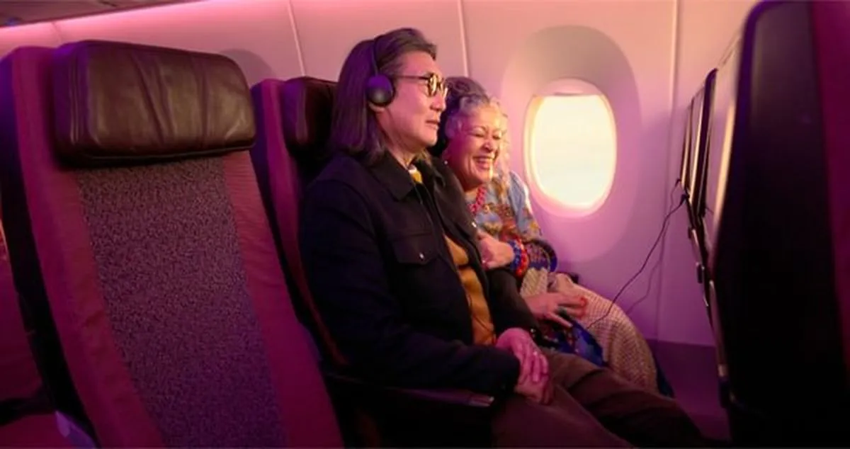 Two people sitting in Virgin Atlantic Economy seats, watching a screen.