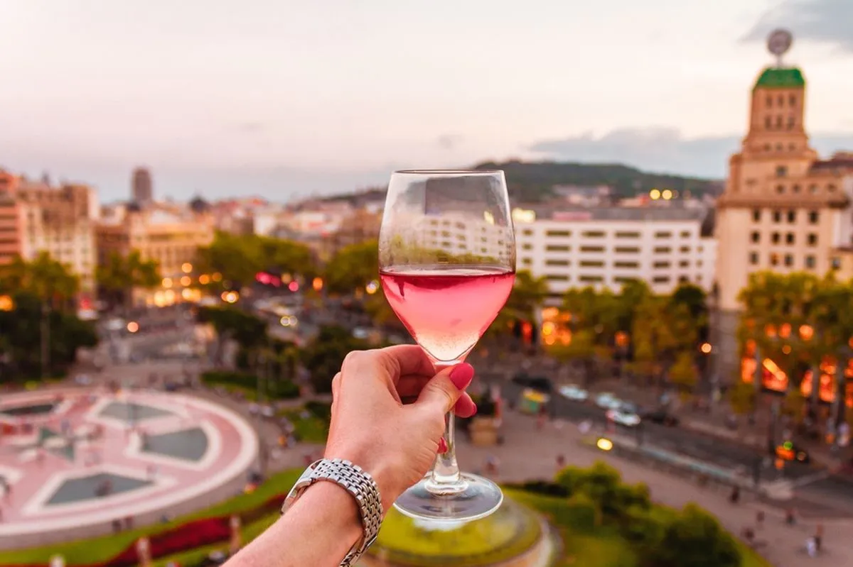 A woman holding a glass of wine in front of a view of Barcelona.