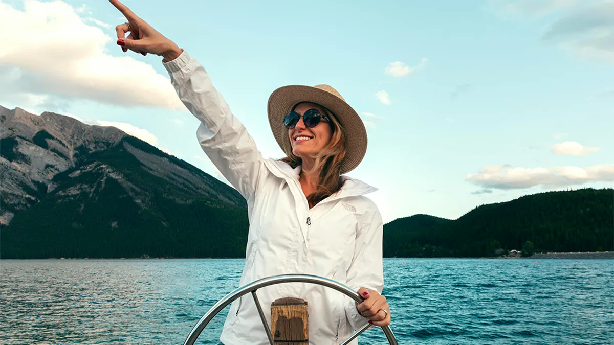 A woman in a white jacket and hat steers a boat