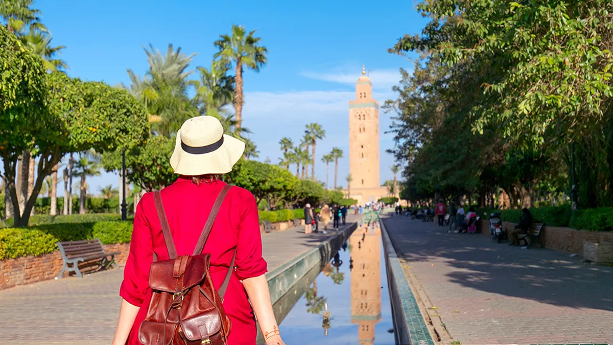 Young woman dressing in red with hat looking the mosque of Koutoubia in Marrakesh
