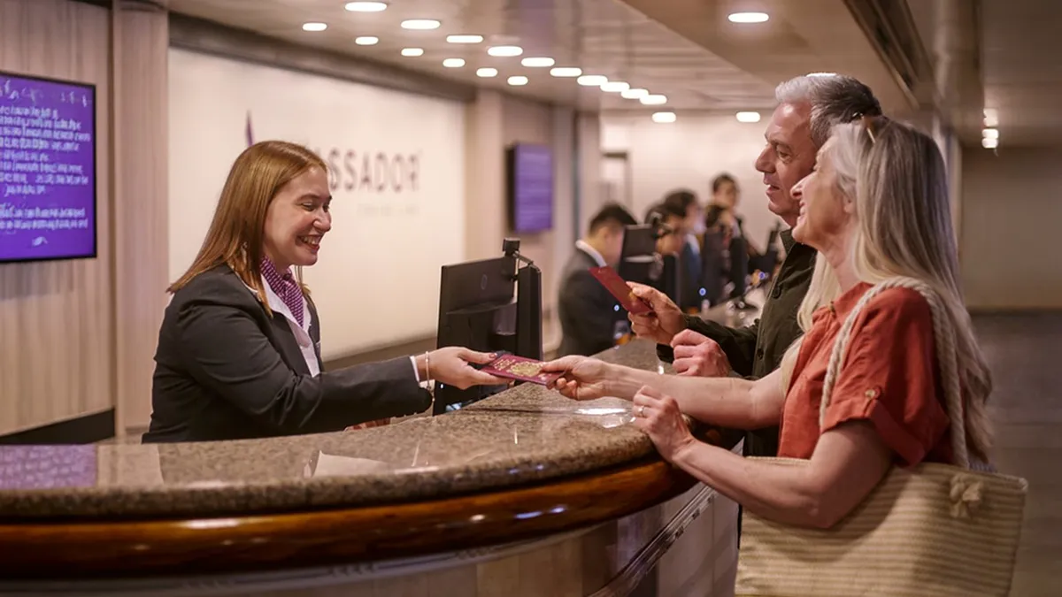 A receptionist hands documents to a smiling couple at the front desk.
