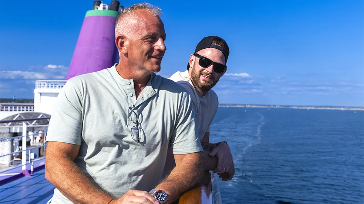 Graham and Lewis smiling and leaning on a ship's railing under a clear blue sky