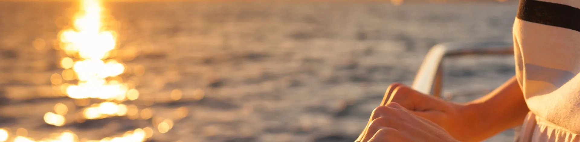 Close up of female hands holding the barrier on a cruise ship during sunset