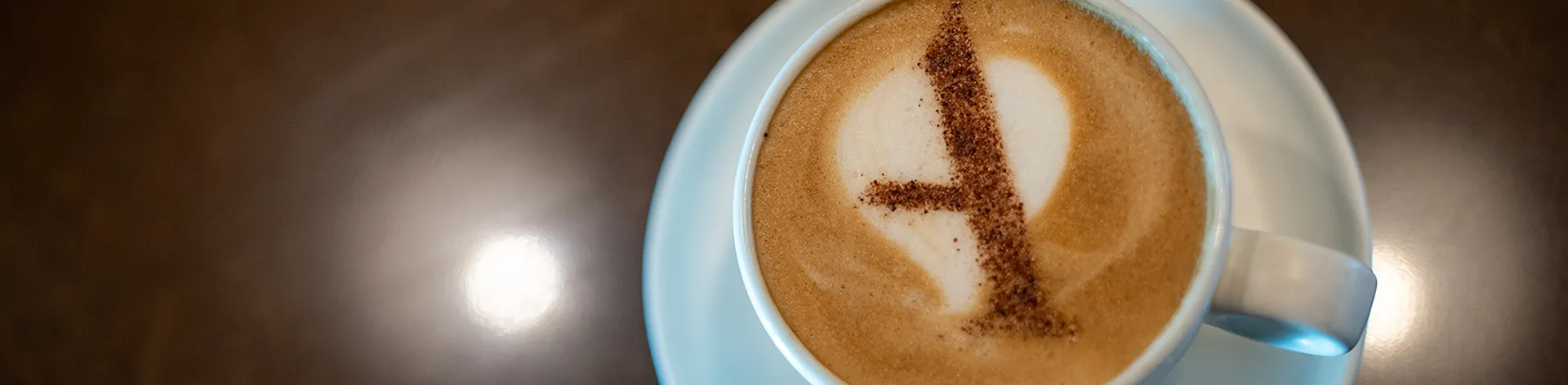 A cup of cappuccino with a heart-shaped design in the foam, served on a saucer against a dark background.