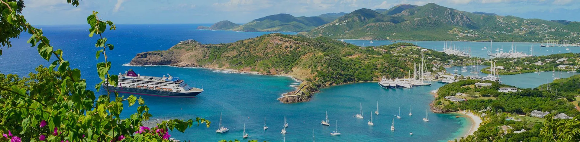 Scenic view of a coastal bay with a cruise ship, sailboats, lush green hills, and clear blue waters under a partly cloudy sky.