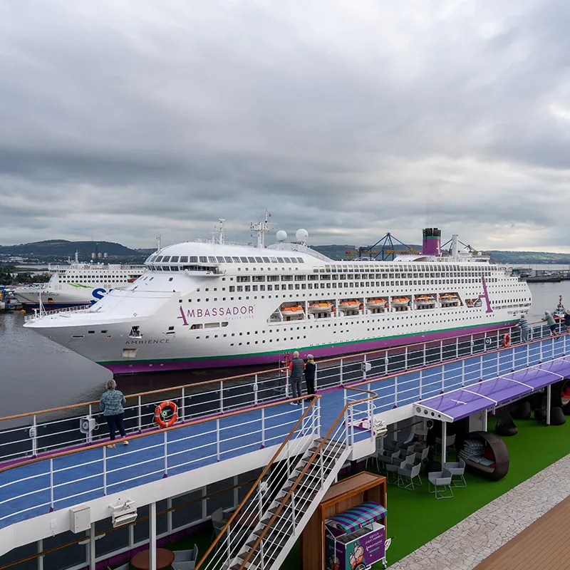 Ambience docked at a port, with a cloudy sky and distant hills in the background.