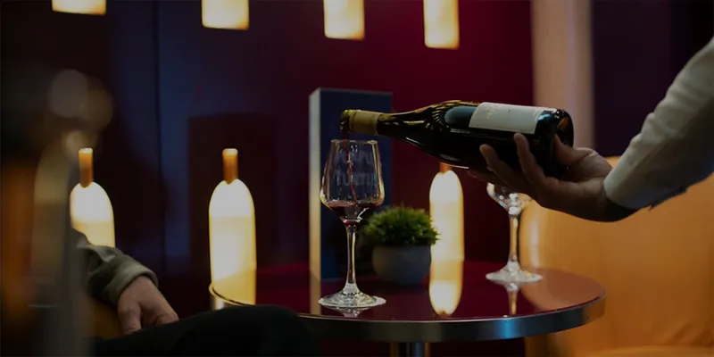 Person pouring red wine into a glass on a small table