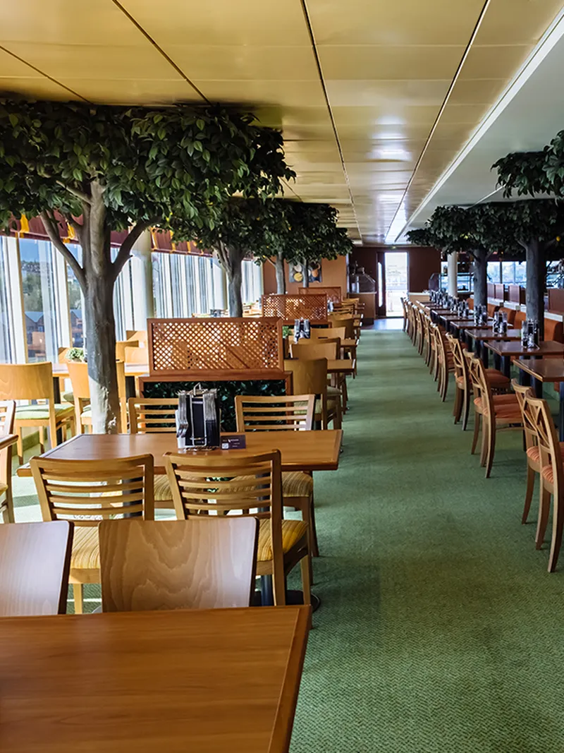 Spacious Borough Market interior with wooden tables and chairs, green carpet, and artificial trees lining the windows.