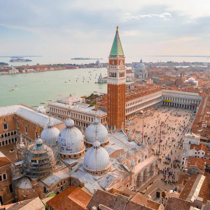 Aerial view of Venice, featuring the Campanile, domes of St. Mark's Basilica, and the surrounding cityscape with the lagoon.