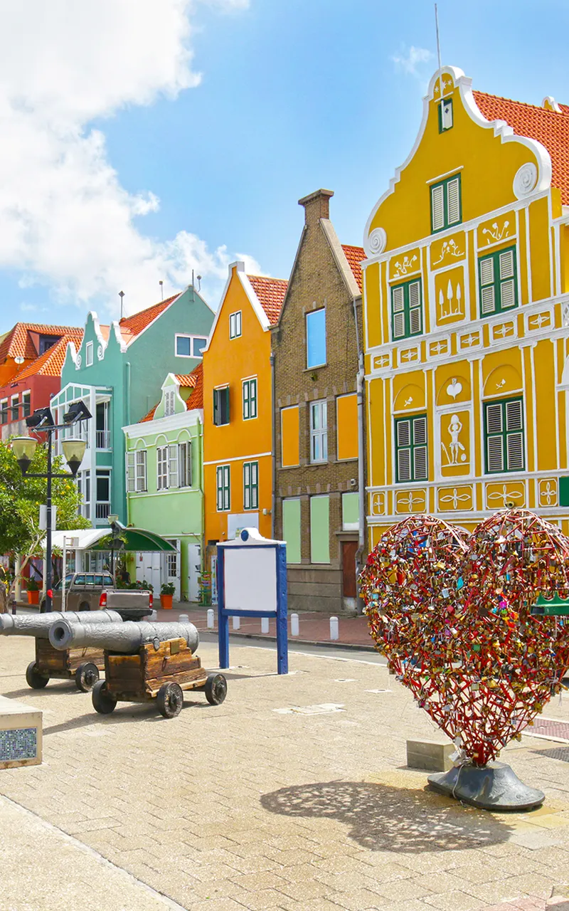 Colorful buildings with a heart-shaped sculpture covered in locks and an old cannon on a sunny day.