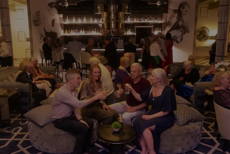 A group of people sitting in a Raffles lounge bar, toasting with drinks.
