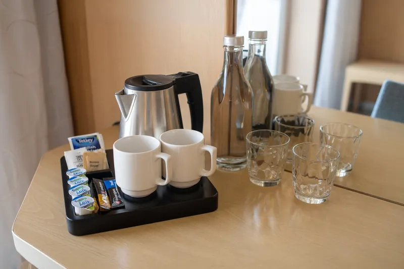 Tray with two white mugs, a kettle and bottled water with glasses on a wooden table