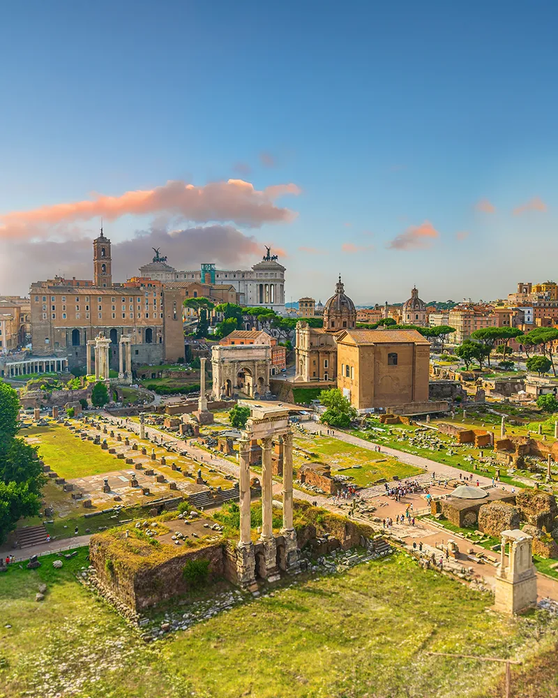 Ancient Roman ruins of the Forum with historic structures, columns, and greenery under a vibrant sky, showcasing Rome's architectural heritage.