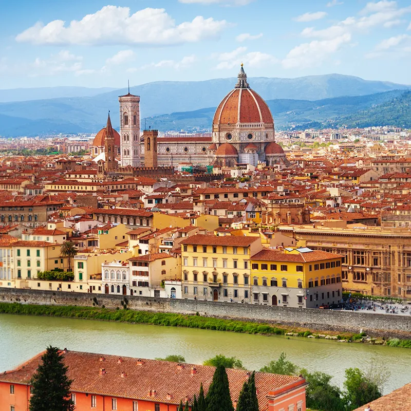 Scenic view of Florence in Italy, city buildings, and distant hills under a blue sky with clouds.