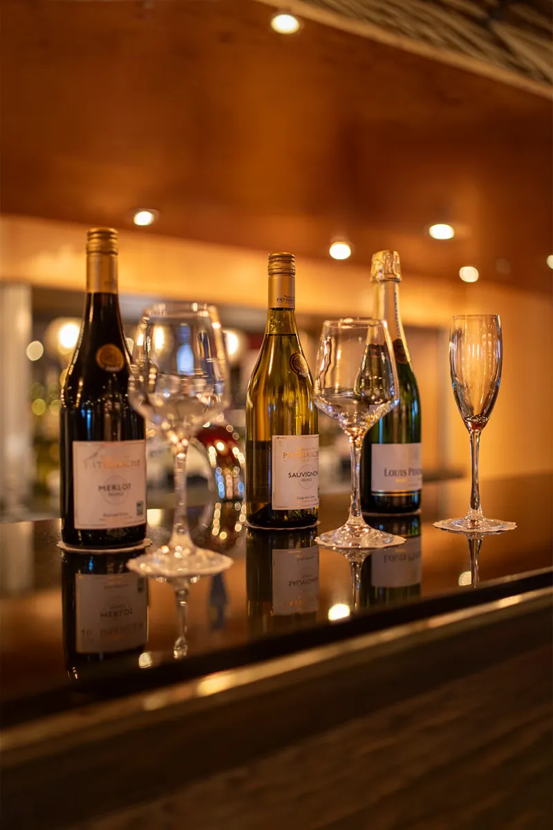 Three wine bottles and four empty glasses on a bar counter