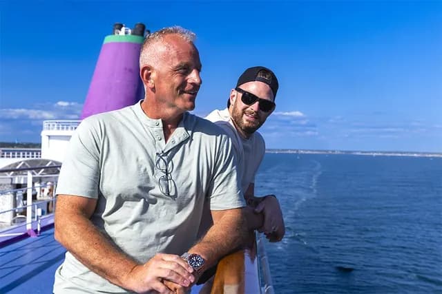 Graham and Lewis smiling and leaning on a ship's railing under a clear blue sky