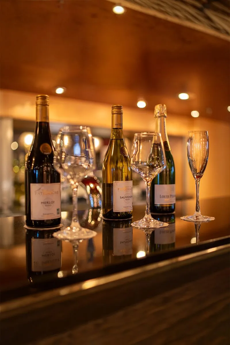 Three wine bottles and four empty glasses on a bar counter