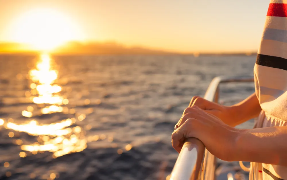Close up of female hands holding the barrier on a cruise ship during sunset