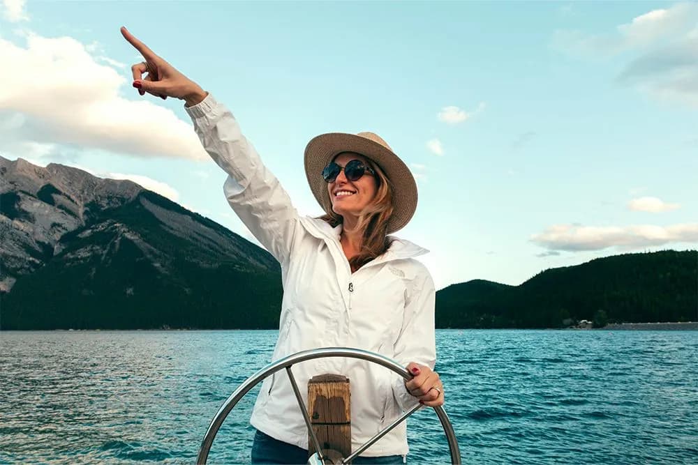 A woman in a white jacket and hat steers a boat