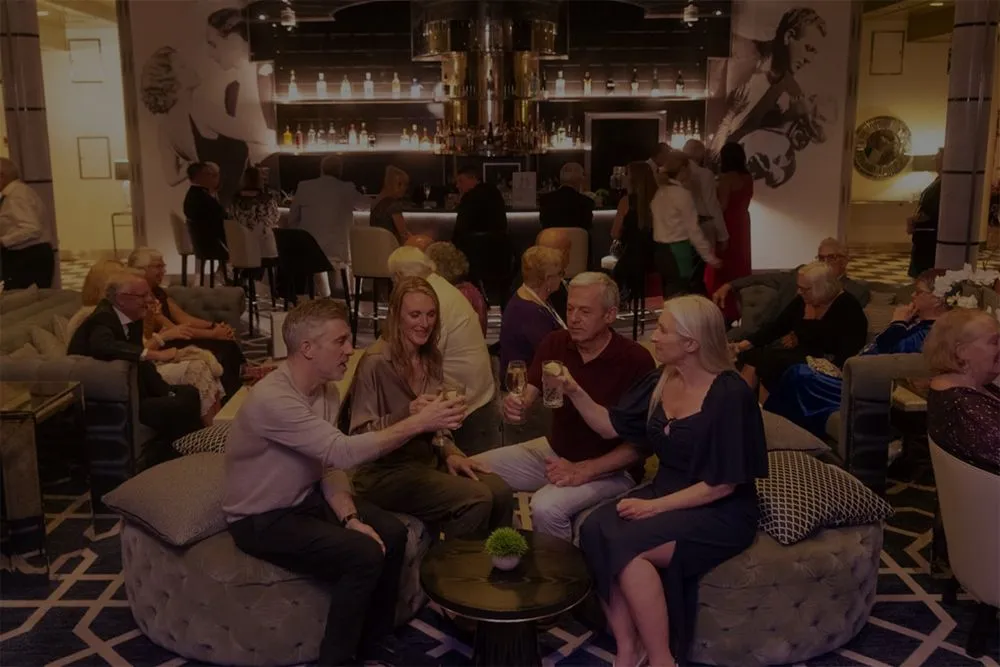 A group of people sitting in a Raffles lounge bar, toasting with drinks.