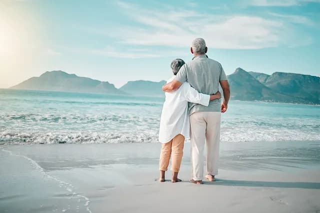 Mature couple hugging on a warm beach looking out to sea