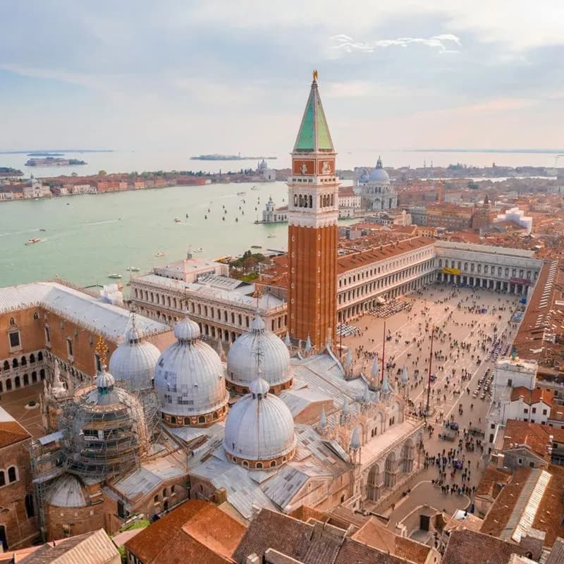 Aerial view of Venice, featuring the Campanile, domes of St. Mark's Basilica, and the surrounding cityscape with the lagoon.