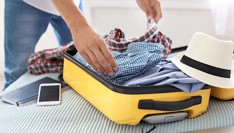 A person packing a yellow suitcase
